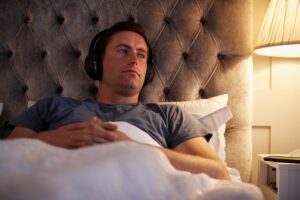 Man Wearing Wireless Headphones Listening To Music Or Podcast Before Going To Sleep